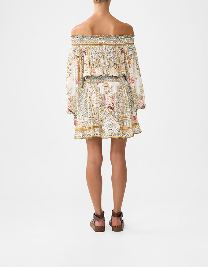 Woman wearing a patterned off-shoulder top on a white background. Ottoman Dynasty Off The Shoulder Short Dress