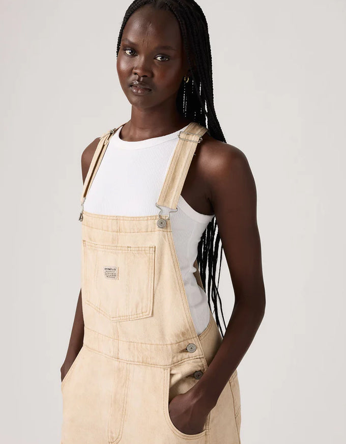 Woman wearing beige overalls over a white tank top on a plain background. Vintage Overall Cloudy Travertine