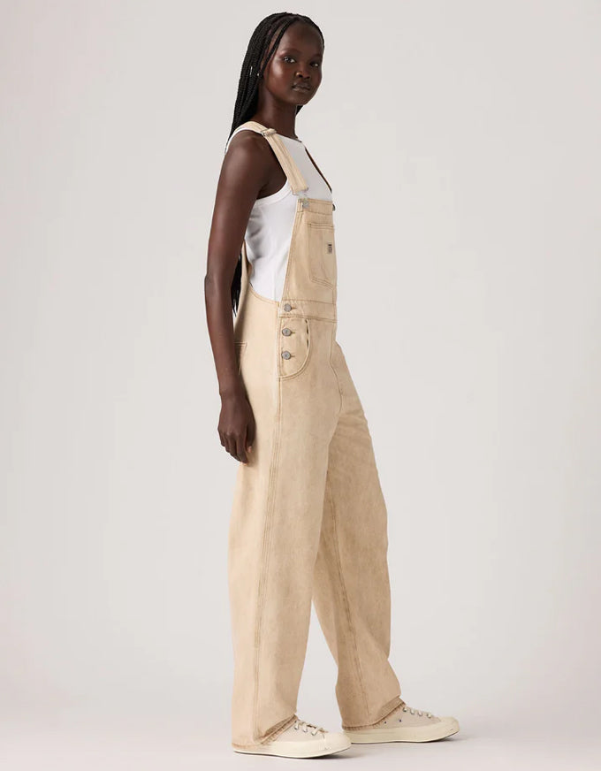 Woman wearing beige overalls and white top on a plain background. Vintage Overall Cloudy Travertine