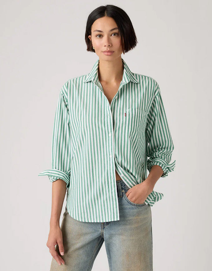 Woman wearing a green and white striped shirt with rolled-up sleeves on a plain background