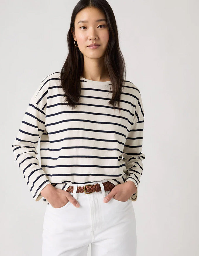 Woman wearing a black and white striped sweater with white pants on a plain background