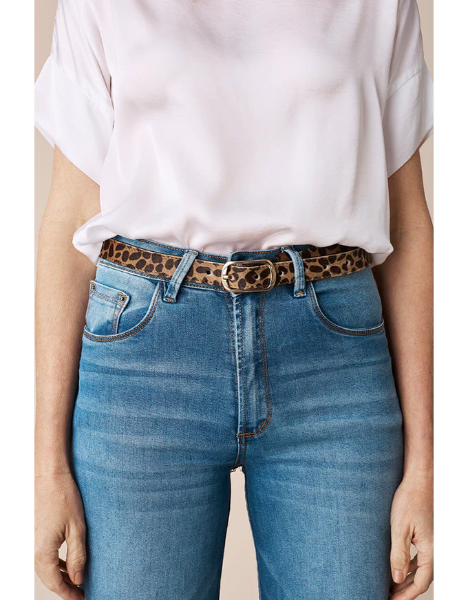 Person wearing blue jeans with a leopard print belt and a white shirt.