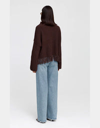 A model shown from the back wearing a dark brown fringed knit sweater and light blue wide-leg jeans against a plain light gray background.