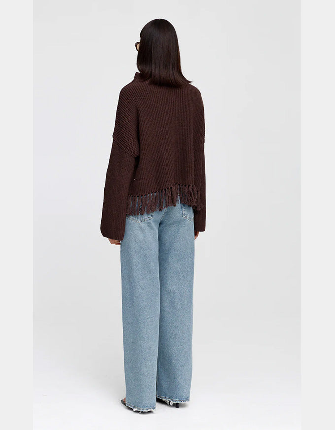 A model shown from the back wearing a dark brown fringed knit sweater and light blue wide-leg jeans against a plain light gray background.