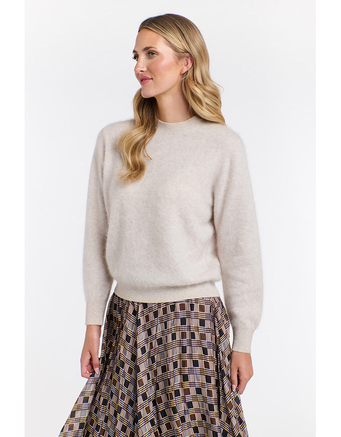 Woman wearing a beige sweater and patterned skirt on a white background