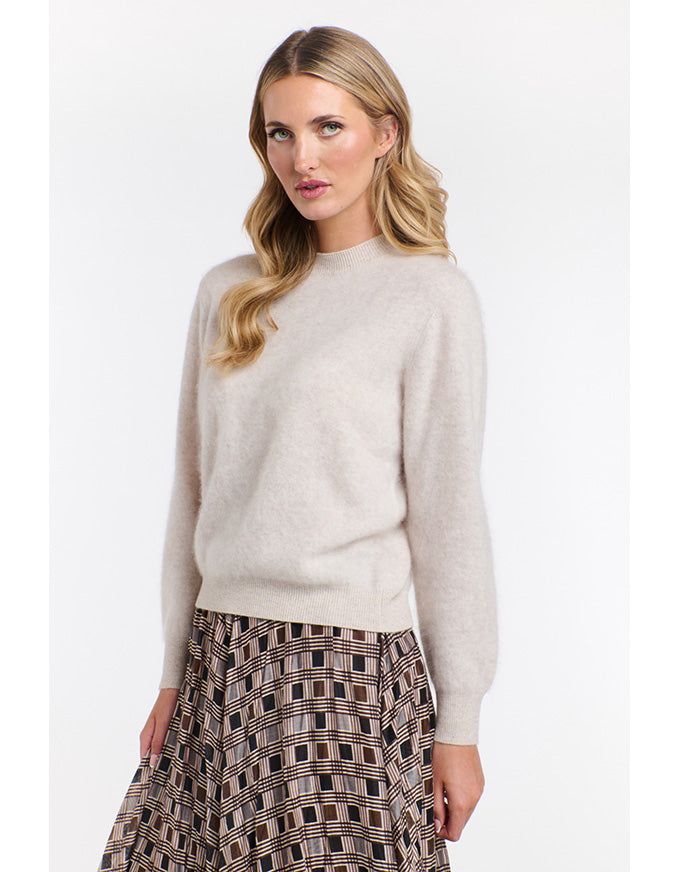 Woman wearing a beige sweater and patterned skirt on a white background