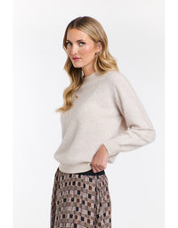Woman wearing a beige sweater and patterned skirt on a white background