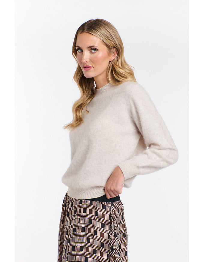 Woman wearing a beige sweater and patterned skirt on a white background