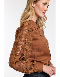 Woman wearing a brown blouse with floral lace details on a white background