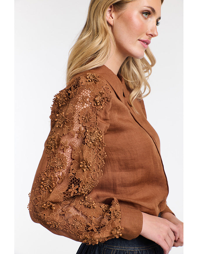 Woman wearing a brown blouse with floral lace details on a white background