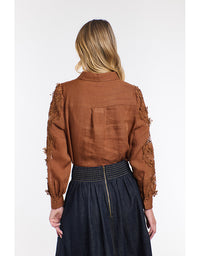 Person wearing a brown blouse with lace sleeves on a white background