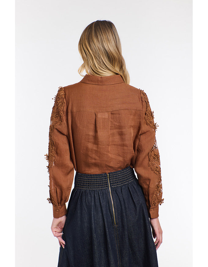 Person wearing a brown blouse with lace sleeves on a white background
