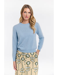 Woman wearing a light blue sweater and patterned skirt on a white background