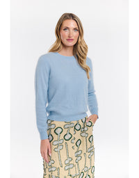 Woman wearing a light blue sweater and patterned skirt on a white background