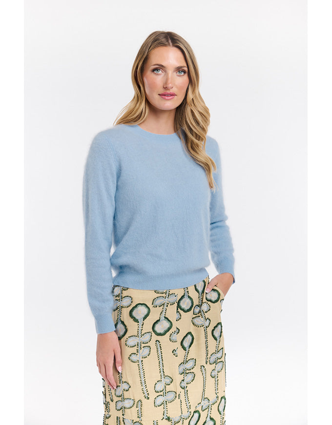 Woman wearing a light blue sweater and patterned skirt on a white background