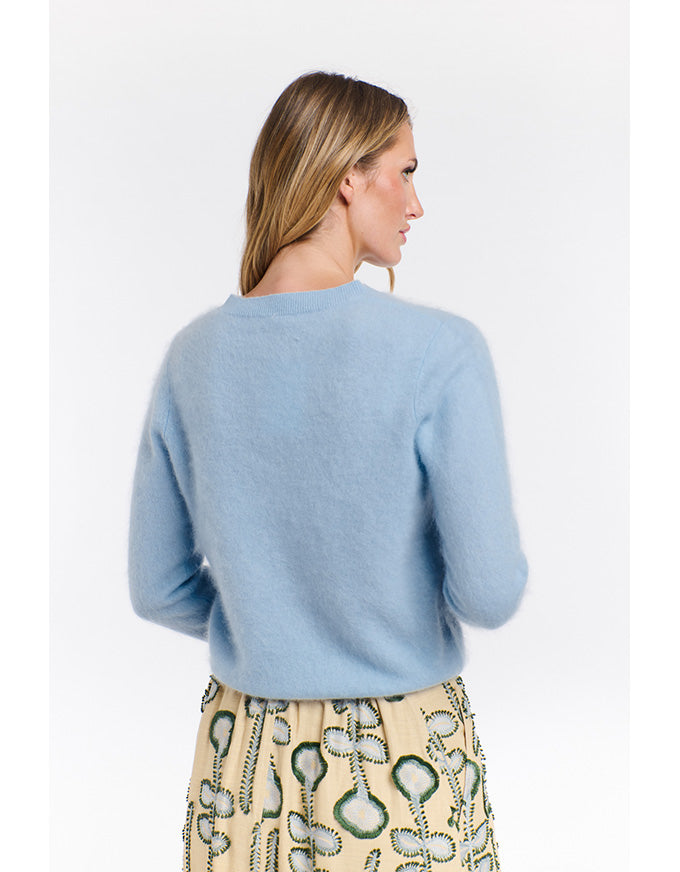 Woman wearing a light blue sweater and patterned pants on a white background