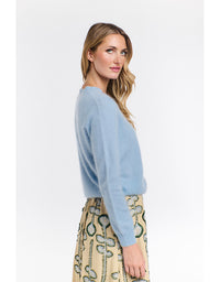 Woman wearing a light blue sweater and patterned skirt on a white background