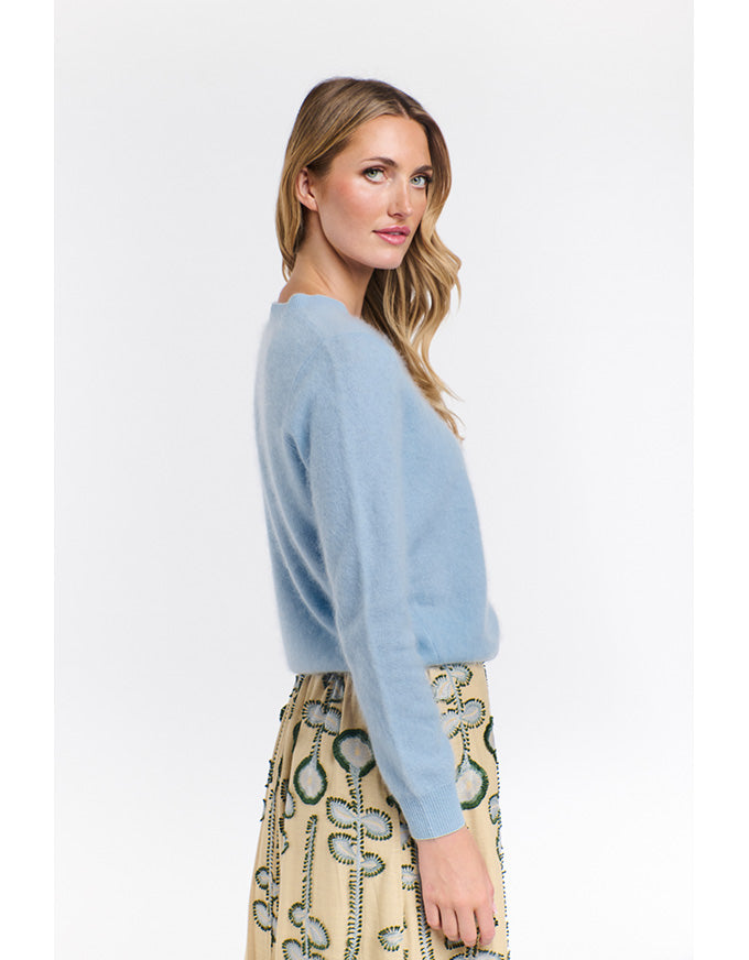 Woman wearing a light blue sweater and patterned skirt on a white background