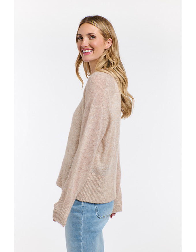 Woman wearing a beige sweater and blue jeans on a white background