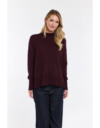 Woman wearing a dark red sweater and dark jeans on a white background