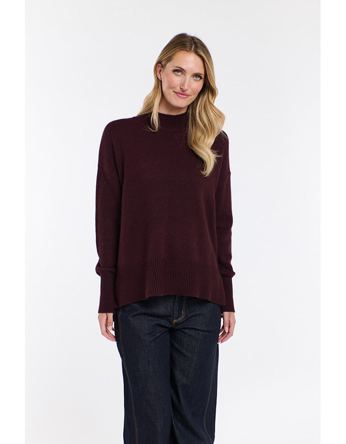 Woman wearing a dark red sweater and dark jeans on a white background