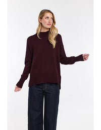 Woman wearing a dark red sweater and dark jeans on a white background