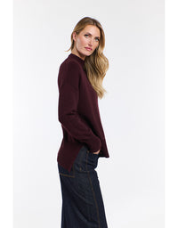 Woman wearing a burgundy sweater and dark jeans on a white background
