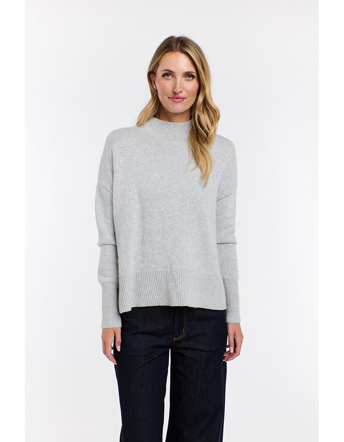 Woman wearing a light gray sweater and dark jeans on a white background