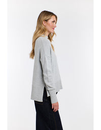 Woman wearing a light gray sweater and dark pants on a white background