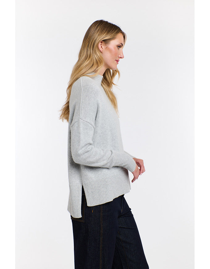 Woman wearing a light gray sweater and dark pants on a white background