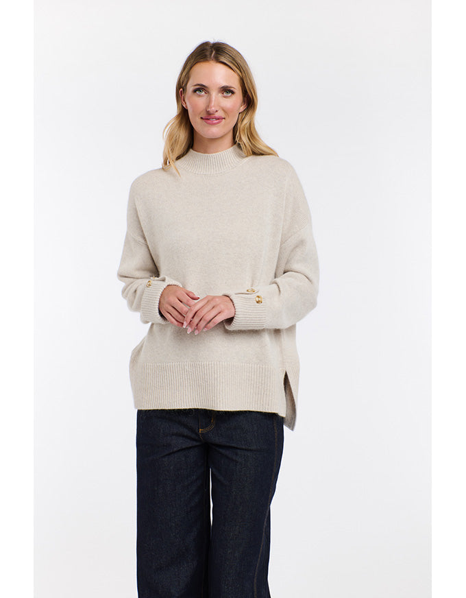 Woman wearing a beige sweater and dark jeans on a white background
