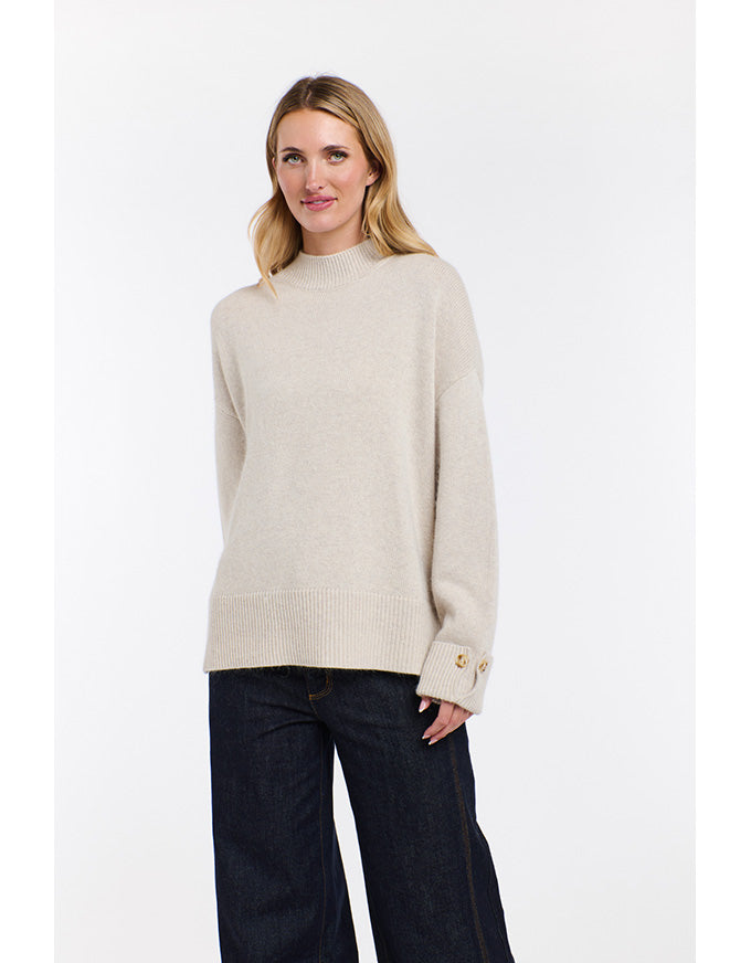 Woman wearing a beige sweater and dark jeans on a white background