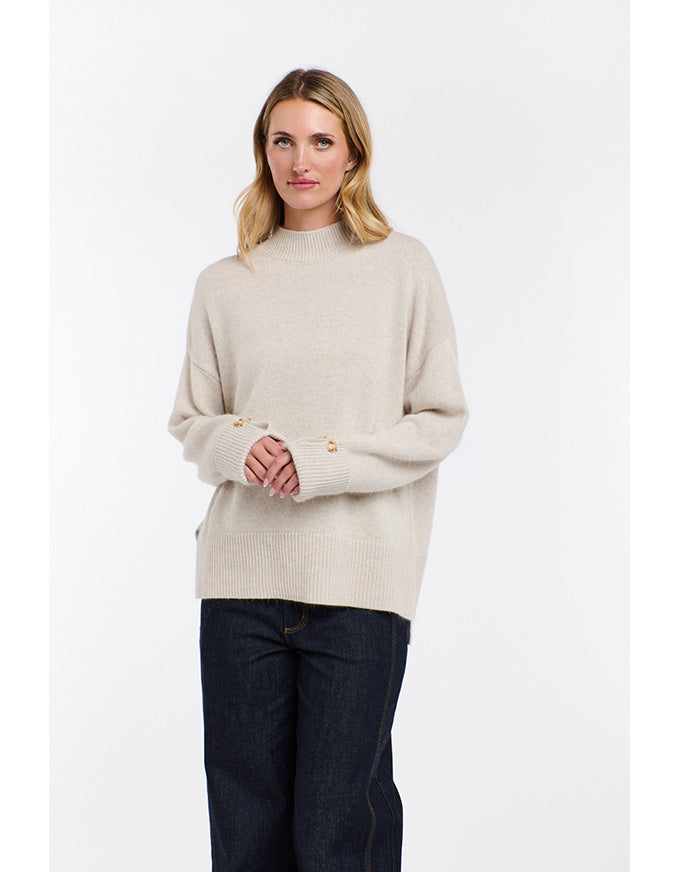 Woman wearing a beige sweater and dark jeans on a white background