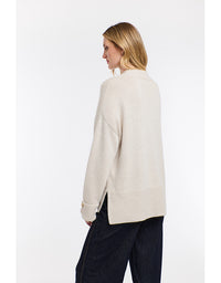 Woman wearing a cream-colored sweater and dark pants on a white background