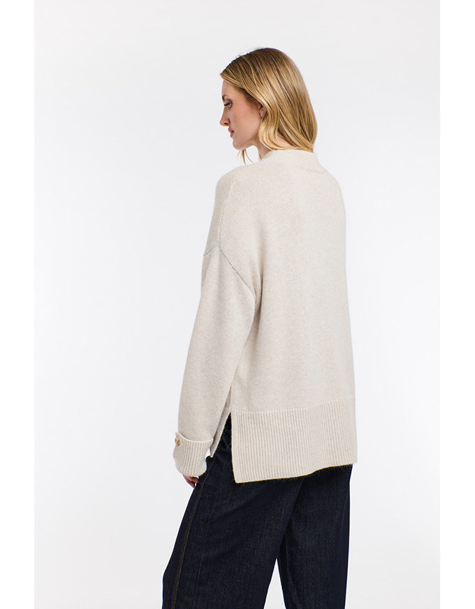 Woman wearing a cream-colored sweater and dark pants on a white background