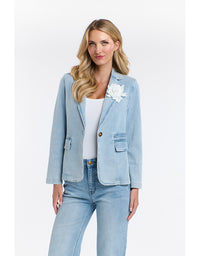 Woman wearing a light blue denim jacket with a white flower accessory on a white background