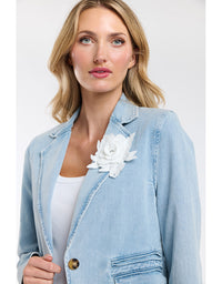 Woman wearing a light blue denim jacket with a white floral accessory on a plain background