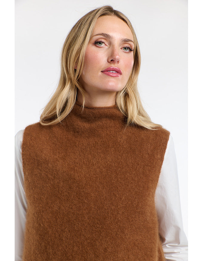 Woman wearing a brown knitted vest over a white shirt on a light background