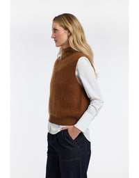 Woman wearing a brown vest over a white shirt on a light gray background