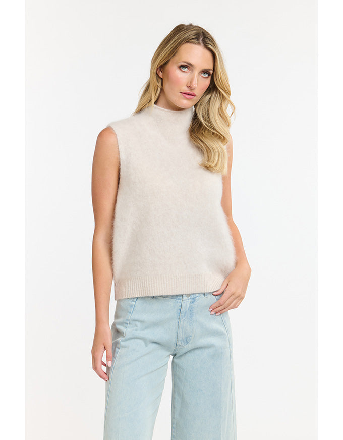 Woman wearing a beige sleeveless sweater and light blue jeans on a white background