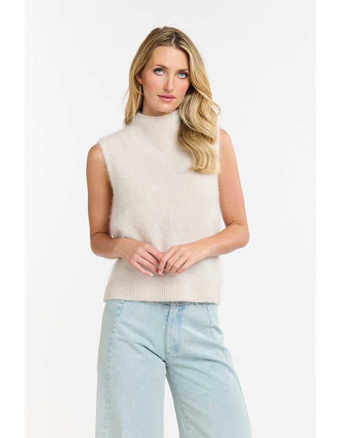 Woman wearing a beige sleeveless sweater and light blue jeans on a white background