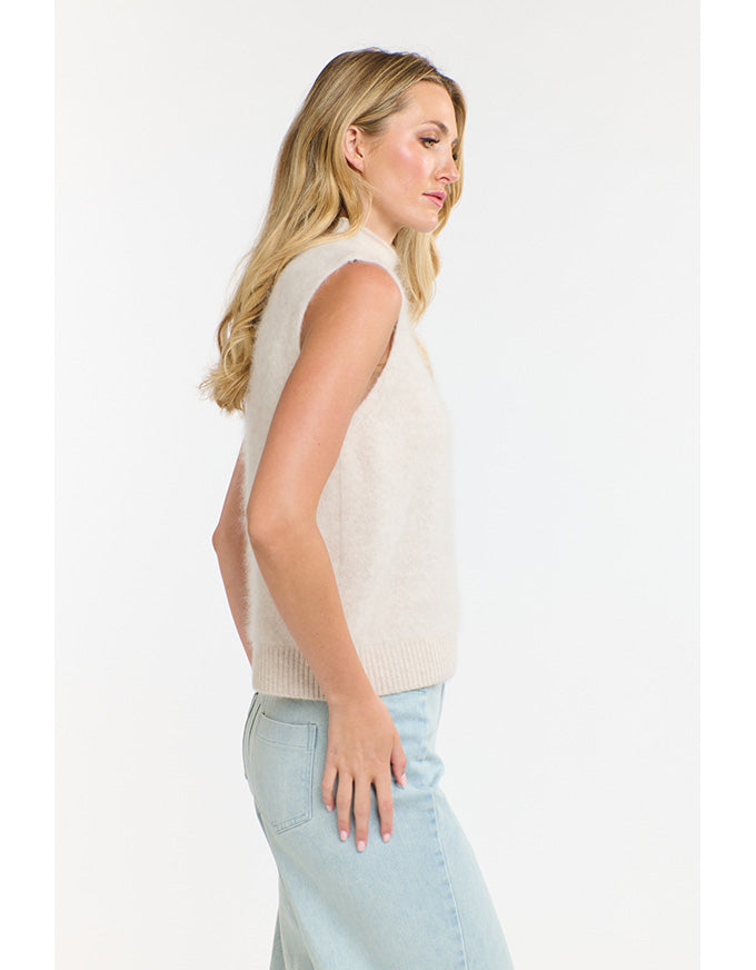 Woman wearing a sleeveless beige top and light blue jeans on a white background