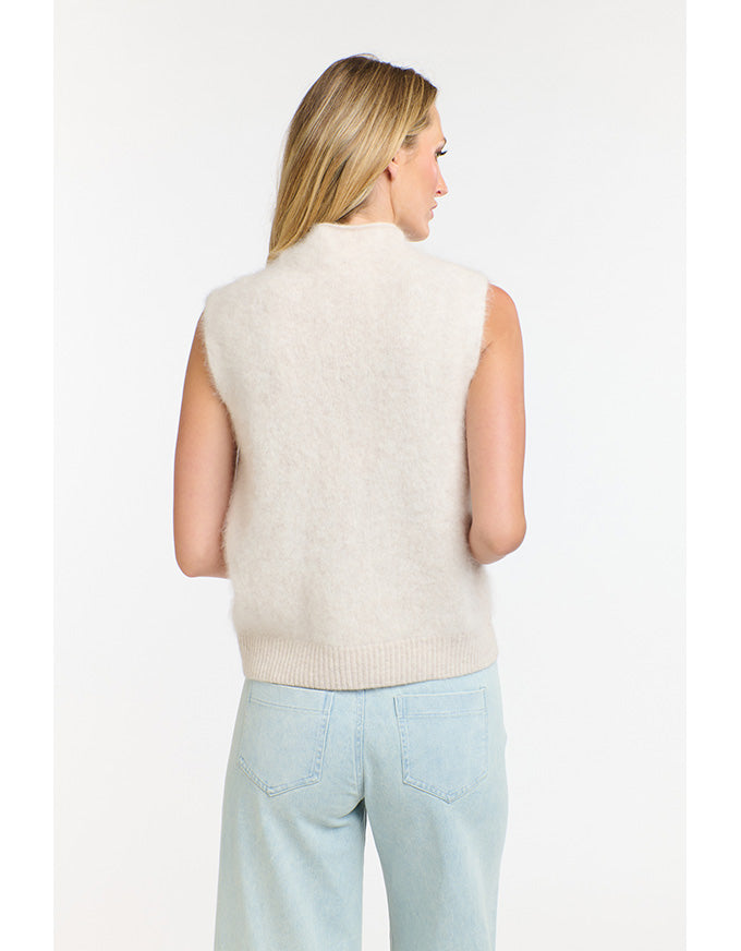 Woman wearing a cream sleeveless sweater against a white background