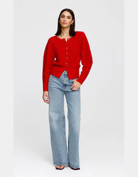 A woman modeling a bright red long-sleeve knit cardigan with a buttoned henley-style neckline, paired with light-wash wide-leg jeans, against a plain light gray studio background.