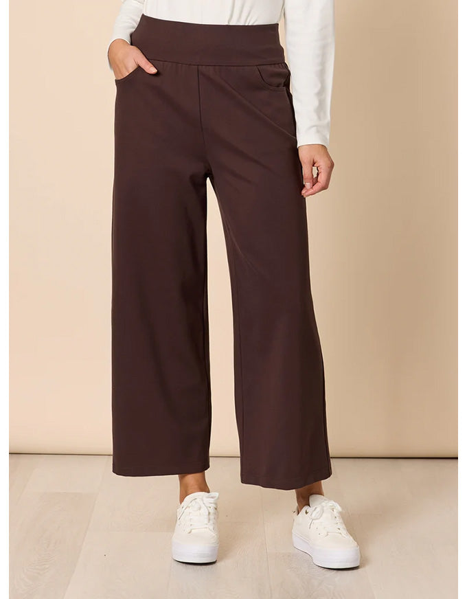Brown wide-leg pants worn with a white shirt and white sneakers on a beige background
