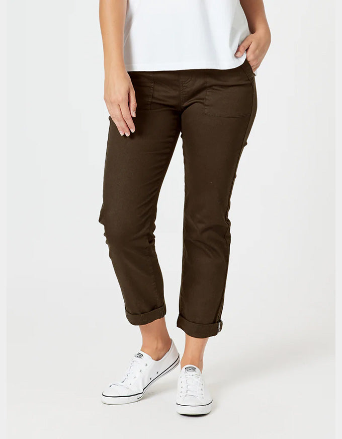 A person wearing dark brown cropped pants with rolled cuffs, paired with a white top and white sneakers, photographed against a light gray studio background.