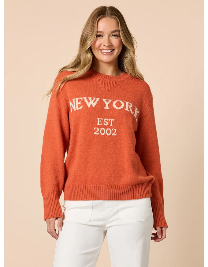 Woman wearing an orange sweater with 'New York Est 2002' text on a beige background