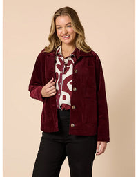 Woman wearing a burgundy jacket over a patterned shirt on a beige background