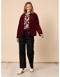 Woman wearing a burgundy jacket, patterned shirt, black pants, and white sneakers on a beige background