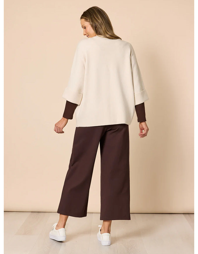Woman wearing a white top and brown pants against a beige background